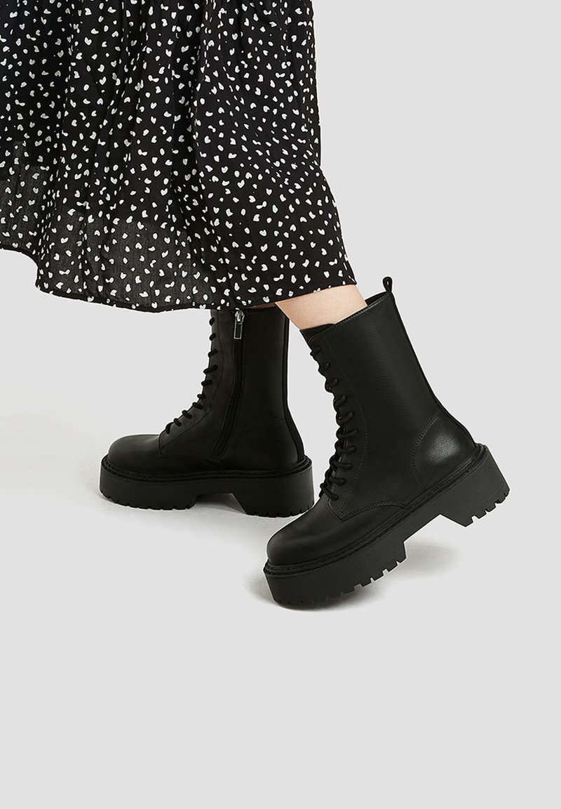 Czarne skórzane botki za kostkę na masywnej platformie, z bocznym zamkiem błyskawicznym i wiązaniem z przodu. Gładka faktura z solidnym bieżnikiem.