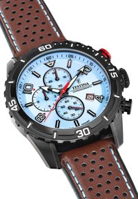 Chronografas su apvaliu juodu korpusu, šviesiai mėlynu ciferblatu, rudos perforuotos odos juostele, raudonais akcentais ir sidabro spalvos valandų žymekliais.