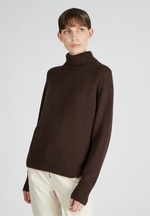 Jersey de cuello alto marrón hecho de material suave, con mangas largas y puños acanalados, de corte relajado, combinado con pantalones de color claro.