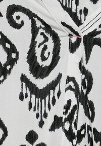 Tela en blanco y negro con un patrón de paisley, con líneas curvas y gotas. Textura suave con un ligero brillo y costuras visibles.