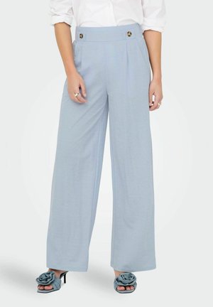 Pantalons larges bleu clair à taille haute avec deux boutons décoratifs, associés à des sandales grises à glisser avec un accent en rose.