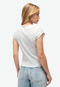 Camiseta gris acanalada con mangas cortas con volantes y dobladillo festoneado, combinada con jeans de color azul claro. La tela parece suave y casual.