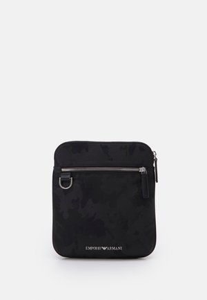Sac bandoulière noir Emporio Armani avec poche avant zippée, fermeture éclair argentée, petite bague métallique et logo en bas au centre.