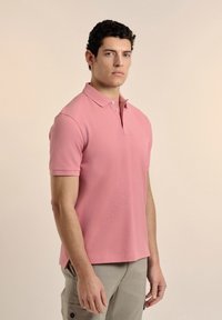 Camisa polo rosa de tejido suave, con cuello clásico, mangas cortas y dobladillo recto, combinada con pantalones cortos tipo cargo beige.