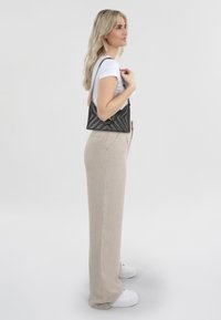 Zwarte gequiltde crossbodytas met een driehoekige vorm, gouden hardware, gecombineerd met beige linnen wijde broek en witte sneakers.