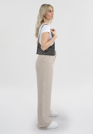 Borsa a tracolla nera trapuntata con forma triangolare, hardware dorato, abbinata a pantaloni a gamba larga in lino beige e sneakers bianche.