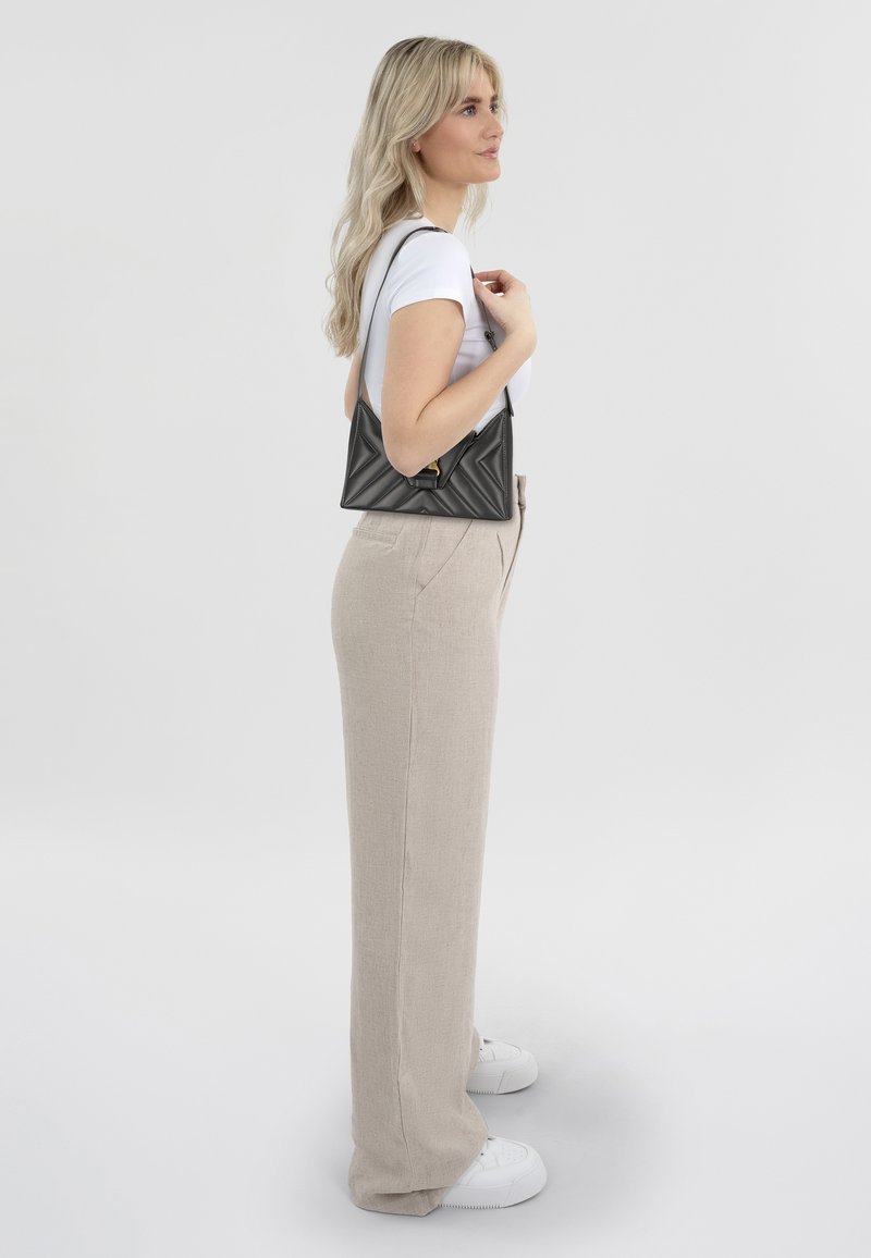 Zwarte gequiltde crossbodytas met een driehoekige vorm, gouden hardware, gecombineerd met beige linnen wijde broek en witte sneakers.