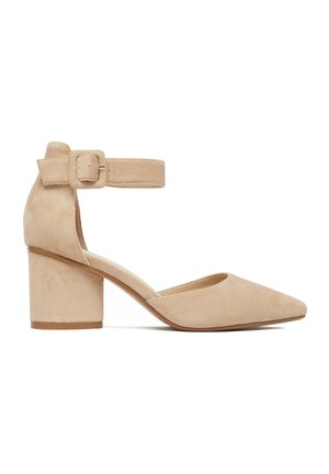 Beżowy damski but na słupku z zamszu z ostrym noskiem i paskiem wokół kostki z kwadratową klamrą.