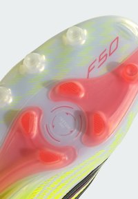 Εξωτερική σόλα παπουτσιού ποδοσφαίρου F50 με διαφανή πλαστική βάση, φωτεινές κίτρινες λεπτομέρειες, κόκκινες προεξοχές πρόσφυσης και κυκλικό σχέδιο πέλματος.