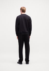 Sort sæt bestående af sweatshirt og bukser med en glat overflade, ribbede manchetter og et enkelt design, båret af en person set fra ryggen.