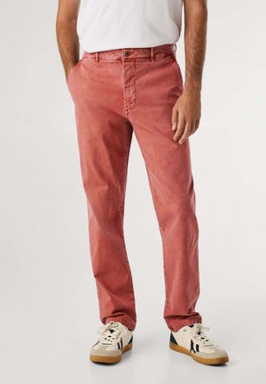 Pantaloni rossi in cotone con una vestibilità comoda, dotati di tasche frontali e chiusura a bottone. Abbinati a sneaker crema e una maglietta bianca.