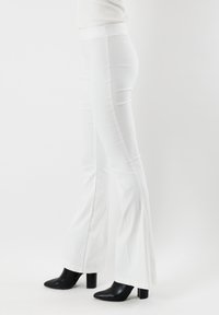 Pantaloni flare bianchi in denim, con una trama liscia e vita alta. Abbinati a scarpe con tacco a blocco nere.