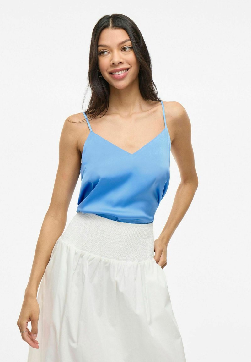 Svetlomodrý saténový top s tenkými ramienkami a výstrihom do V, kombinovaný s bielou sukňou s gumičkovým pásom a nariasenou textúrou.