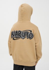 Felpa con cappuccio di colore marrone chiaro, con una grande grafica nera "NARUTO" sulla schiena, caratterizzata da una vestibilità comoda e una texture morbida.