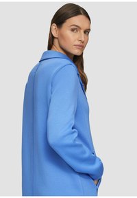Giacca blu con colletto strutturato, maniche lunghe e tasche laterali. Realizzata in tessuto texturizzato, presenta un design pulito e su misura.