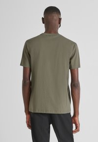 Camiseta de algodón verde oliva con manga corta y cuello redondo; textura suave, diseño simple y corte recto en el dobladillo.
