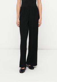 Μαύροι ριμπ παντελόνες με φαρδιά μπότα και ελαστική μέση, με λεία υφή και άνετη εφαρμογή. Συνδυασμένοι με μαύρα φλατ παπούτσια.