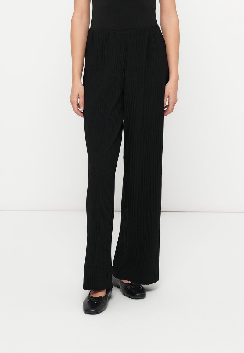 Μαύροι ριμπ παντελόνες με φαρδιά μπότα και ελαστική μέση, με λεία υφή και άνετη εφαρμογή. Συνδυασμένοι με μαύρα φλατ παπούτσια.