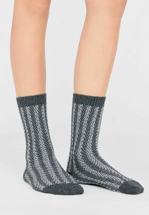 Piernas con calcetines gruesos de punto de lana hasta la mitad de la pantorrilla con rayas diagonales grises y blancas y puños y punteras sólidos grises.