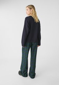 Laivastonsininen ylipitkä neule, jossa on ribbireunus, yhdistettynä vihreisiin ja sinisiin ruudullisiin leveälahkeisiin housuihin, jotka tarjoavat pehmeän tuntuman ja rentoa istuvuutta.