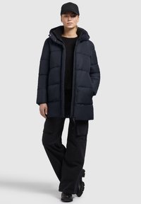 Navy quilted puffer jacket with a drawstring hood and zipper closure. Paired with black cargo pants and chunky black boots.
