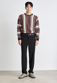 Pruhovaný pletený svetr v barvách bordó, béžové a černé, doplněný úzkými černými kalhotami. Kompletní s šedými botami a černým opaskem.