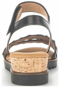 Sandalo in pelle nera con tacco in sughero, soletta imbottita color tan e cinturini regolabili. Presenta un accento in sughero testurizzato sul tacco.