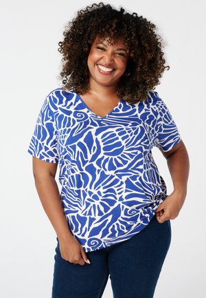 Korte mouwen, V-hals top in het wit met blauwe abstracte bloempatronen. Zachte stof, ontspannen pasvorm met een lichte draping. Gepaard met donkere denim.