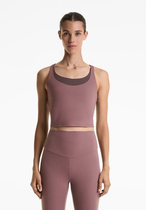 Mauve sportski crop top s širokim naramenicama i okruglim izrezom, u kombinaciji s tajicama visokog struka, oboje izrađeno od rastezljivog, glatkog materijala.