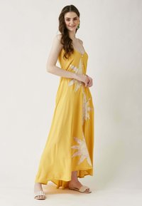 Gelbes Maxikleid mit Spaghettiträgern, Frontknöpfen und großer weißer Blumenstickerei auf einer Seite. Weicher Stoff mit fließendem Design.
