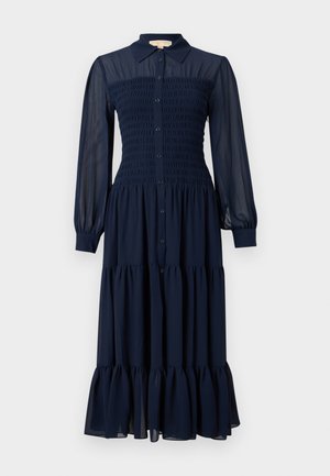 Robe longue bleu marine avec col Claudine, corsage smocké, boutonnage sur le devant et ourlet à volants à étages ; fabriquée en tissu léger et transparent.