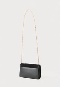 Borsa a mano nera rettangolare con un morbido risvolto superiore e una lunga tracolla sottile in oro su uno sfondo chiaro.