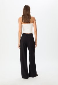 Top bianco senza spalline e pantaloni neri a gamba larga. Il top è aderente, mentre i pantaloni presentano una silhouette comoda e una vita elastica.