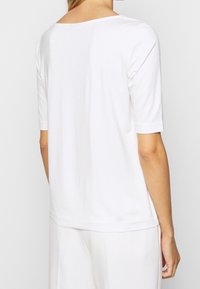 T-shirt blanc à manches courtes en tissu doux, avec un col large et une coupe décontractée, comportant des détails de coutures subtils à l'arrière.