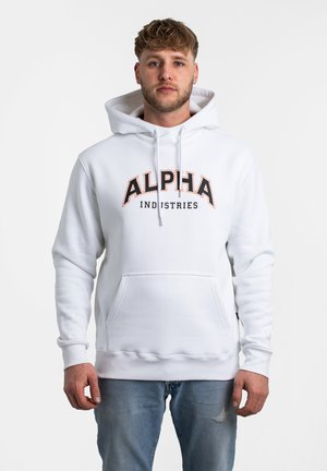 Sudadera blanca con un bolsillo frontal, capucha con cordón y el texto audaz "ALPHA" en negro y naranja. Textura suave, diseño casual, combinada con jeans de color azul claro.