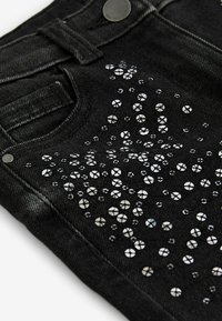 Svarta jeans av denim med ett prickigt mönster av reflekterande rhinestones på ena sidan, vilket ger textur och visuellt intresse.
