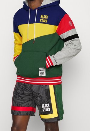 Sudadera multicolor con paneles en azul, amarillo, verde, rojo y gris; cuenta con un bolsillo tipo canguro y un dobladillo de rayas rojas. Pantalones cortos de malla con estampados gráficos.