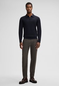 Marineblauwe polo met lange mouwen en ritskraag, gecombineerd met bruine geruite broek en bruine leren laarzen, met een slim fit silhouet en ribgebreide manchetten.