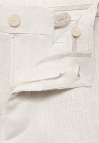 Pantalones de lino blancos con cremallera frontal, dos botones y acentos de bolsillo cosidos a máquina para mayor detalle y funcionalidad.