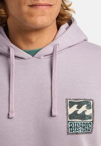 Felpa lilla con cappuccio caratterizzata da un'etichetta in tessuto con un design a onde. I lacci e la tasca a marsupio aggiungono funzionalità.