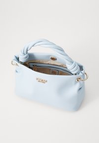 Sac à main Guess bleu clair avec poignée torsadée, logo doré sur le devant et ouverture supérieure montrant une poche intérieure beige zippée.