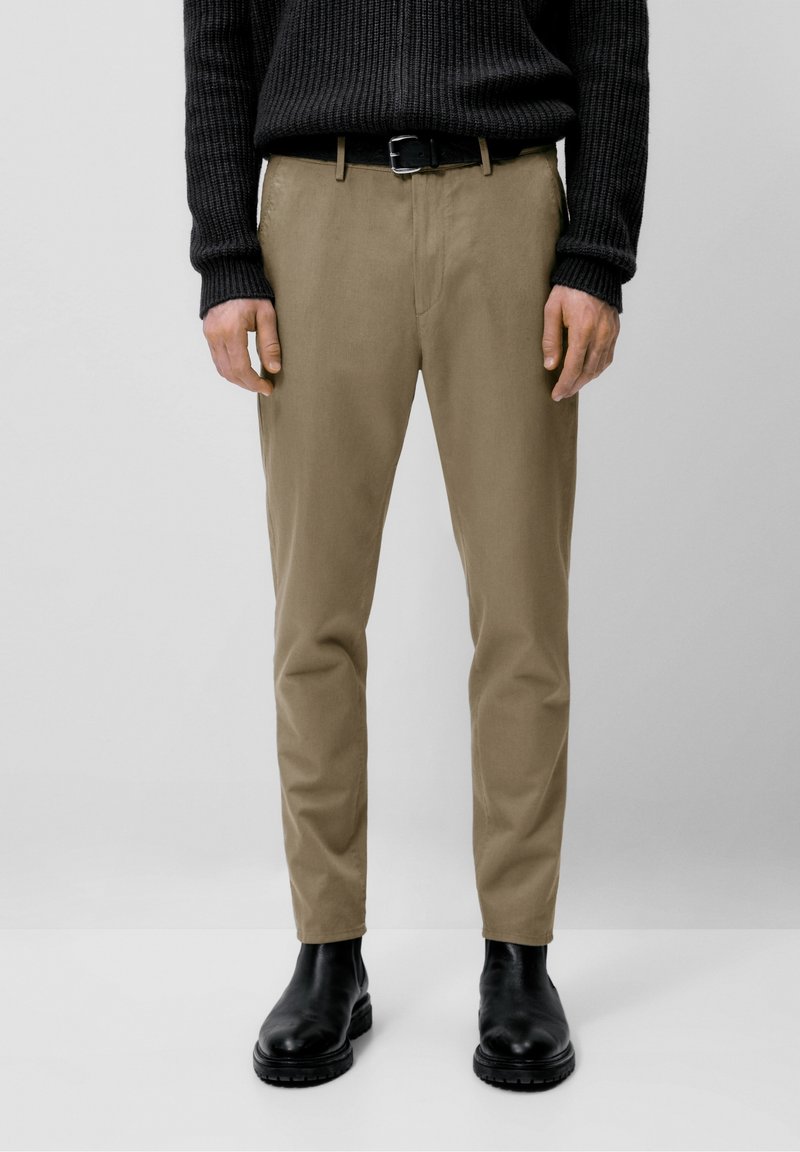 Beige chino's met een slim fit, gemaakt van katoen. Gecombineerd met een zwarte geribde trui en zwarte leren enkellaarsjes.