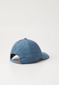Boné de corduroy azul com uma coroa arredondada, aba curvada e faixa ajustável na parte de trás. Apresenta textura ribbed vertical e orifícios de ventilação.