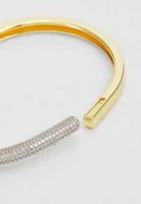 Aukso ir sidabro bangle apyrankė, turinti lygią auksinę dalį ir tekstūruotą sidabrinę dalį, puošiančią žibančiomis akmenimis.