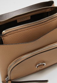 Bolso de cuero marrón con un acabado texturizado, que cuenta con compartimentos con cremallera y acentos de hardware plateado. Incluye una correa desmontable.