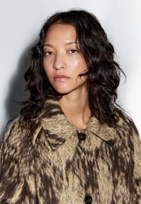 Texturierter Mantel aus einer Mischung von Braun- und Beigetönen mit einem gepunkteten Muster, Rundkragen und schwarzen Knopfverschlüssen.