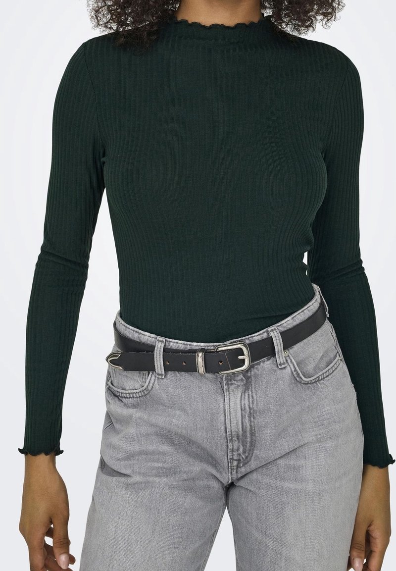 Ciemnozielona prążkowana bluzka z długim rękawem i falbanastym dekoltem, zestawiona z szarymi spodniami o wysokim stanie i czarnym paskiem.