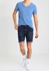 Modrý tričko s výstřihem do V, džínové šortky s ohrnutými lemy, bílé tenisky a bílé ponožky. Neformální letní oblečení s jednoduchým designem.