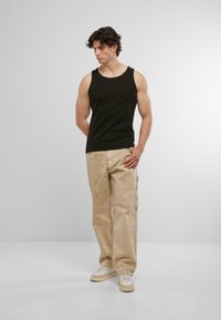 Schwarzes ärmelloses Tanktop kombiniert mit hellbeigen, lockeren Hosen und weißen Sneakern, das ein einfaches, figurbetontes Design und eine glatte Textur aufweist.
