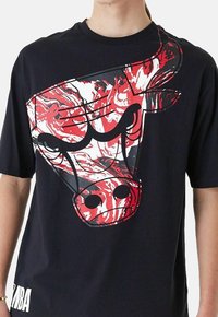 Maglietta nera con una grande grafica di un toro marmorizzato rosso e bianco. Maniche corte, scollo rotondo, con "NBA" stampato in bianco sull'orlo.
